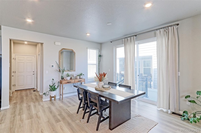 dining space with baseboards, light wood-style flooring, and a textured ceiling