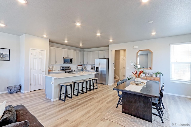 kitchen with an island with sink, a kitchen breakfast bar, stainless steel appliances, light countertops, and light wood-style floors