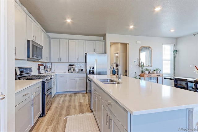 kitchen with tasteful backsplash, appliances with stainless steel finishes, light countertops, light wood-style floors, and a sink