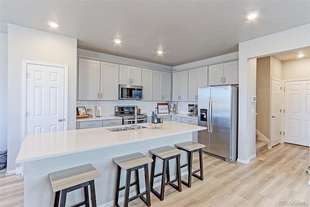 kitchen featuring a breakfast bar area, stainless steel appliances, light countertops, light wood-style flooring, and decorative backsplash