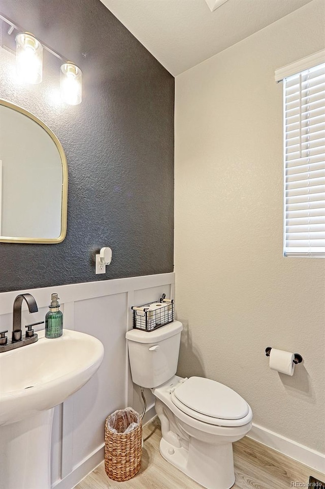 half bathroom featuring a wainscoted wall, toilet, a sink, wood finished floors, and baseboards