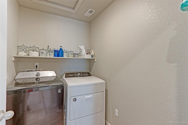 clothes washing area with laundry area, visible vents, a textured wall, and separate washer and dryer