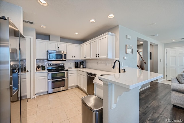 1133 S Richfield St, Aurora, CO 80017 - kitchen featuring stainless steel appliances, a peninsula, tasteful backsplash, white cabinetry, and recessed lighting