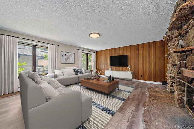 living room with light hardwood / wood-style floors, a textured ceiling, a healthy amount of sunlight, and wooden walls