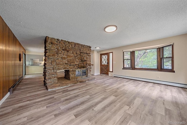 unfurnished living room featuring wooden walls, light hardwood / wood-style flooring, a baseboard radiator, a textured ceiling, and a fireplace