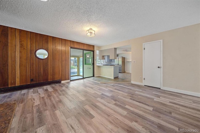 unfurnished living room with light hardwood / wood-style floors, a textured ceiling, and wooden walls