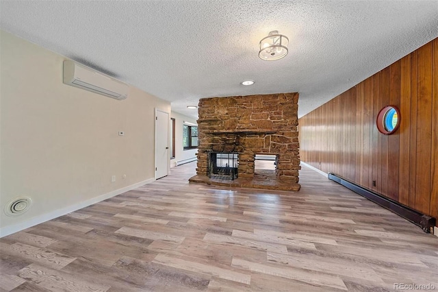 unfurnished living room featuring light hardwood / wood-style floors, a textured ceiling, an AC wall unit, and a baseboard radiator