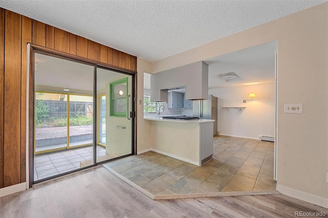 kitchen featuring light hardwood / wood-style flooring, a textured ceiling, baseboard heating, and kitchen peninsula