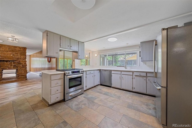 kitchen featuring kitchen peninsula, appliances with stainless steel finishes, a textured ceiling, gray cabinets, and light hardwood / wood-style floors