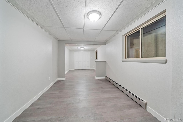 corridor with a paneled ceiling, a baseboard heating unit, and light wood-type flooring