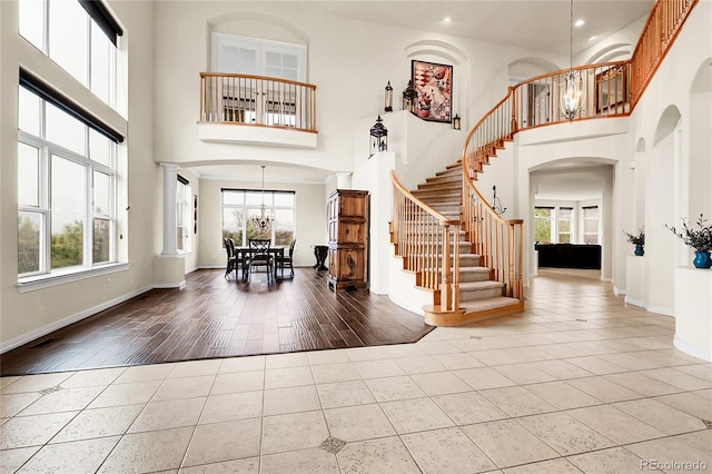 tiled entryway with a chandelier, arched walkways, stairs, a high ceiling, and baseboards