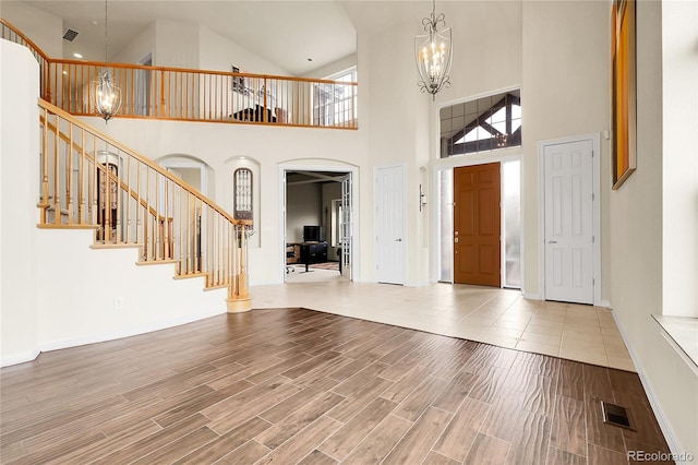 entrance foyer with a chandelier, arched walkways, high vaulted ceiling, stairs, and wood finished floors