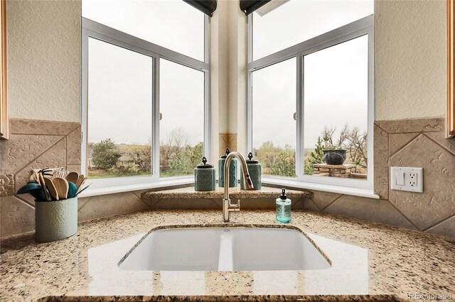 kitchen view of a sink, light stone counters, and a textured wall