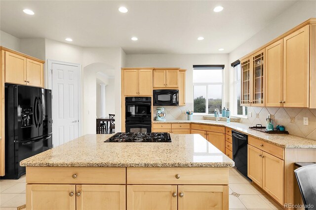 kitchen featuring black appliances, light brown cabinetry, arched walkways, a kitchen island, and decorative backsplash