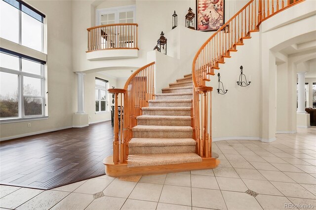 staircase with arched walkways, decorative columns, a towering ceiling, and tile patterned flooring