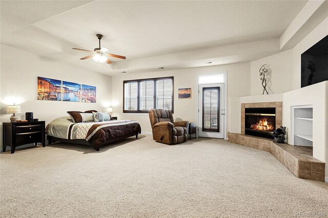 carpeted bedroom featuring a raised ceiling, a tiled fireplace, and a ceiling fan