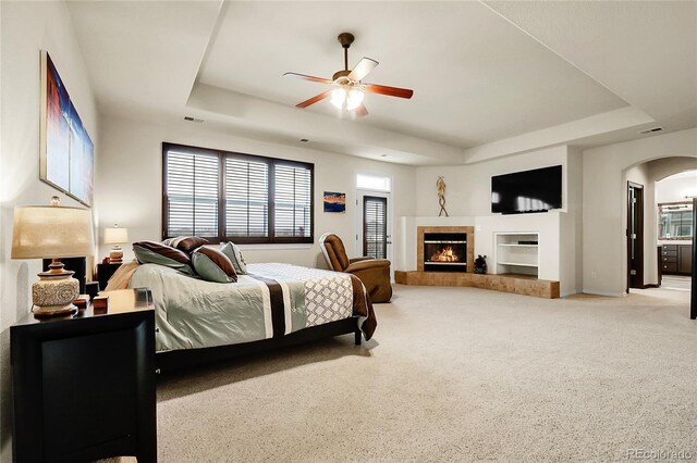 bedroom with a raised ceiling, arched walkways, carpet floors, and a tile fireplace