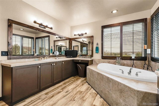 bathroom with wood finished floors, a garden tub, healthy amount of natural light, and vanity