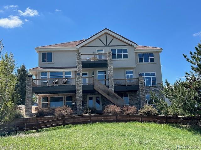 back of house featuring a balcony, stucco siding, stairway, stone siding, and a lawn