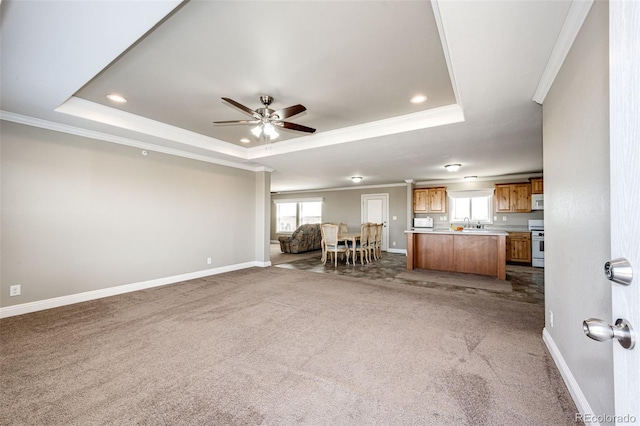 unfurnished living room with ornamental molding, carpet flooring, ceiling fan, and a tray ceiling