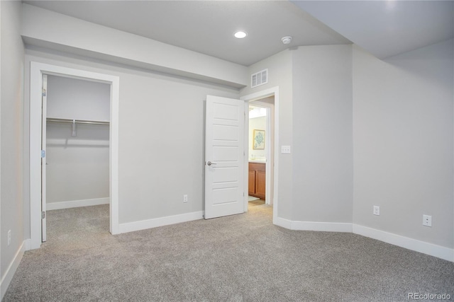 unfurnished bedroom with baseboards, visible vents, recessed lighting, light carpet, and a walk in closet