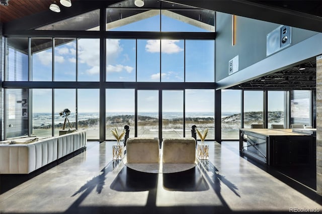 interior space featuring a beach view, high vaulted ceiling, concrete flooring, floor to ceiling windows, and a water view