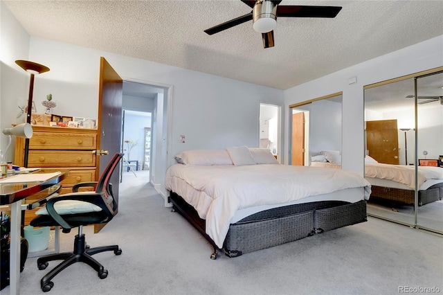 bedroom featuring light carpet, ceiling fan, two closets, and a textured ceiling