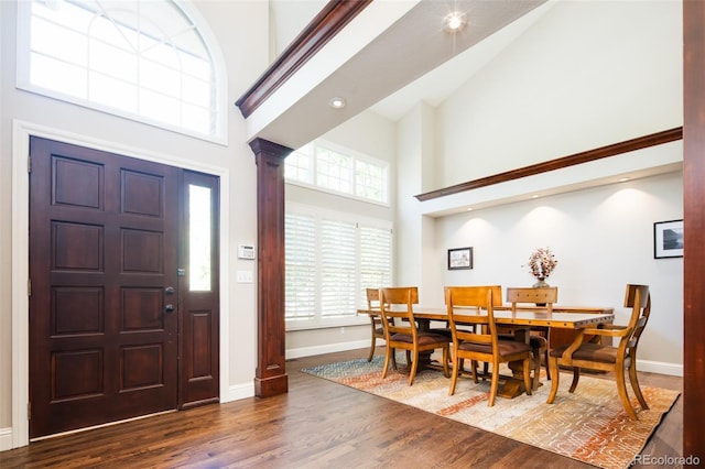 entrance foyer featuring high vaulted ceiling, decorative columns, baseboards, and wood finished floors