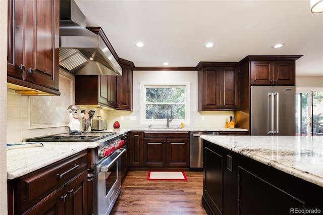 kitchen with light stone countertops, wall chimney exhaust hood, high end appliances, and a sink