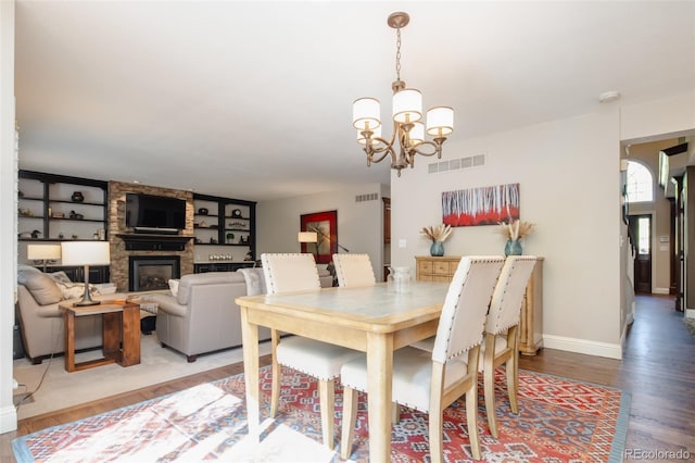 dining area featuring a chandelier, a stone fireplace, visible vents, baseboards, and light wood-type flooring