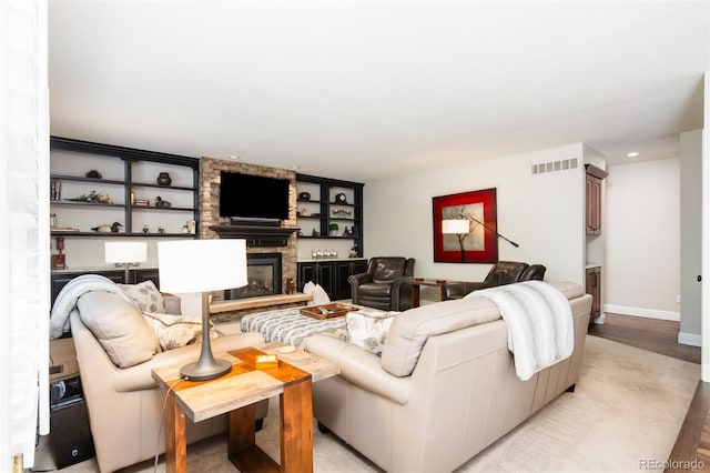 living area with a stone fireplace, visible vents, baseboards, built in features, and light wood-type flooring