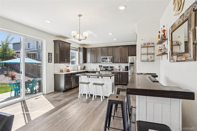 1846 Osprey Dr, Brighton, CO 80601 - kitchen featuring stainless steel appliances, dark brown cabinets, backsplash, light wood-style floors, and a center island