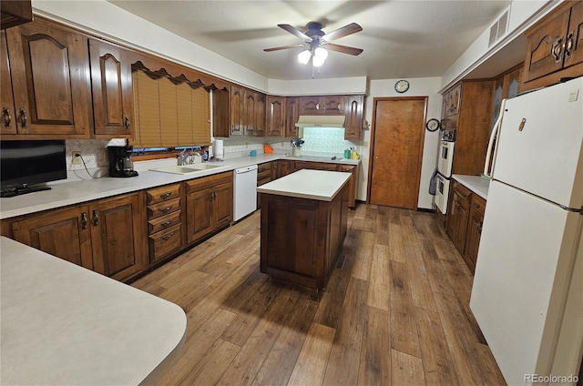 kitchen with white appliances, hardwood / wood-style floors, decorative backsplash, under cabinet range hood, and visible vents