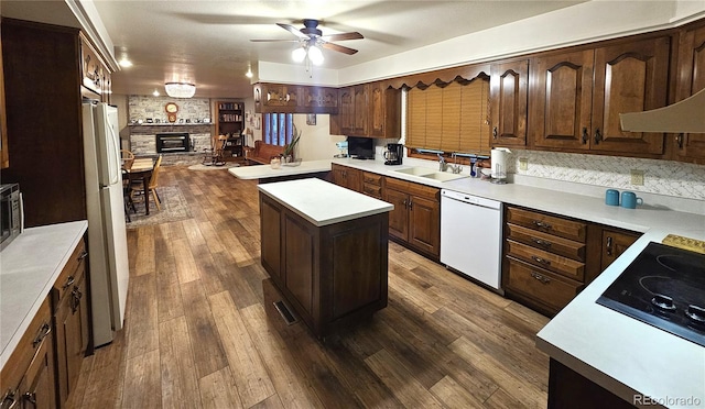 kitchen featuring ceiling fan, a sink, white appliances, a large fireplace, and dark wood-type flooring