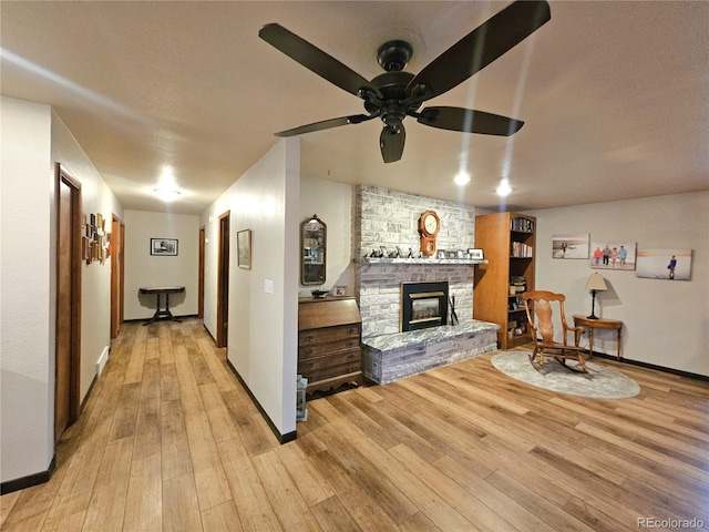 living room featuring light wood-style floors, baseboards, ceiling fan, and a fireplace
