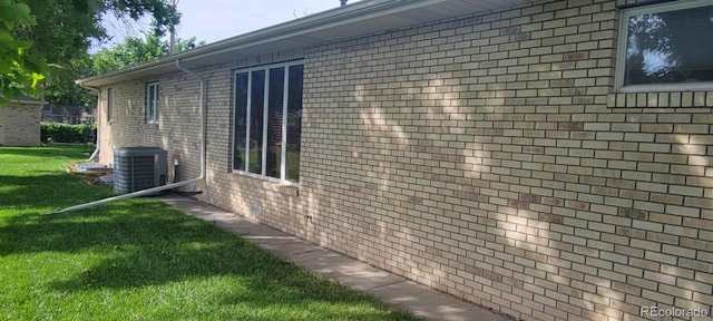 view of side of property with a lawn, brick siding, and central AC unit