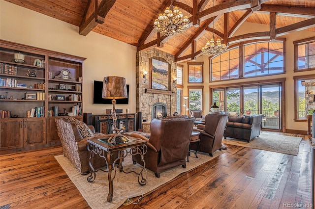 living room featuring a notable chandelier, a stone fireplace, wood-type flooring, and high vaulted ceiling