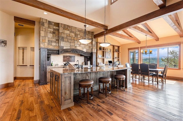 kitchen with beam ceiling, dark hardwood / wood-style flooring, decorative light fixtures, and dark stone counters