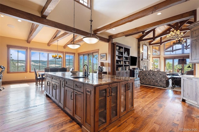 kitchen featuring pendant lighting, dark stone counters, a center island with sink, lofted ceiling with beams, and sink