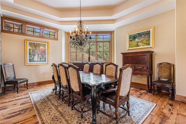 dining room with hardwood / wood-style floors, a tray ceiling, and a notable chandelier