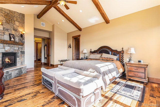 bedroom with beam ceiling, a stone fireplace, ceiling fan, and wood-type flooring