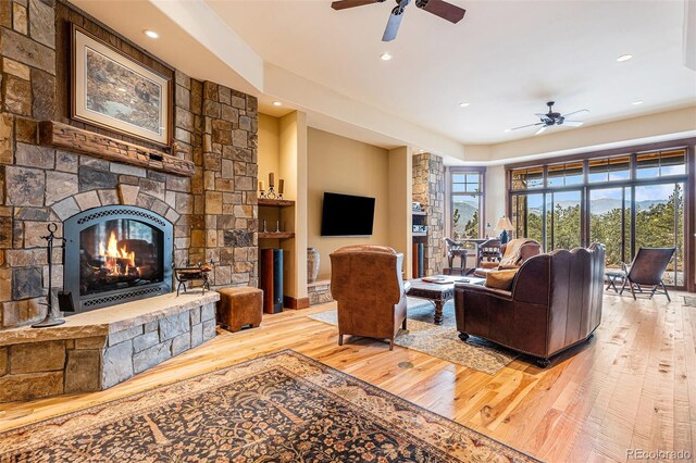 living room featuring a stone fireplace, ceiling fan, and hardwood / wood-style floors