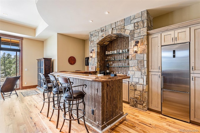 bar featuring light brown cabinets, light hardwood / wood-style flooring, and built in refrigerator