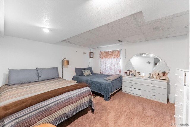 bedroom with a drop ceiling and light colored carpet