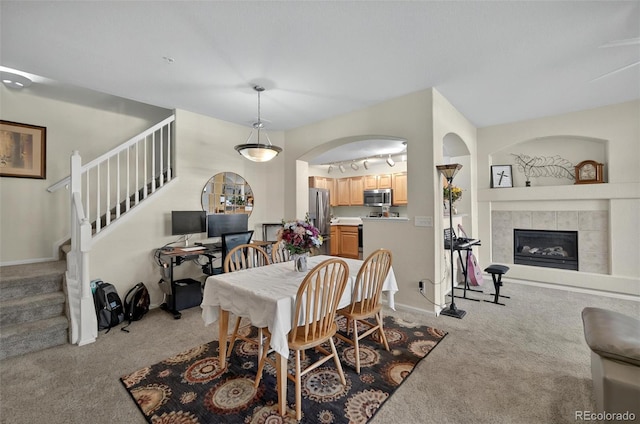 dining area featuring light carpet, stairway, a fireplace, arched walkways, and baseboards