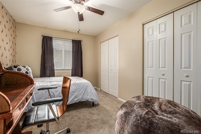 bedroom with ceiling fan, light carpet, and two closets