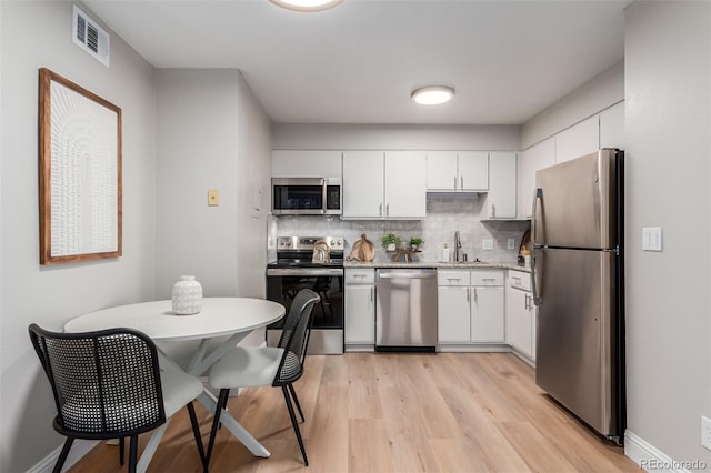 kitchen with appliances with stainless steel finishes, a sink, light wood-style floors, white cabinetry, and decorative backsplash