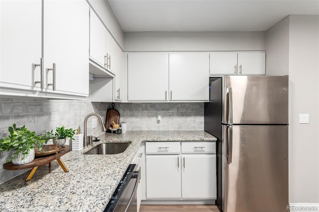 kitchen featuring freestanding refrigerator, a sink, dishwasher, white cabinets, and light stone counters