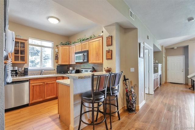 kitchen featuring appliances with stainless steel finishes, light wood-style flooring, a peninsula, a sink, and a textured ceiling