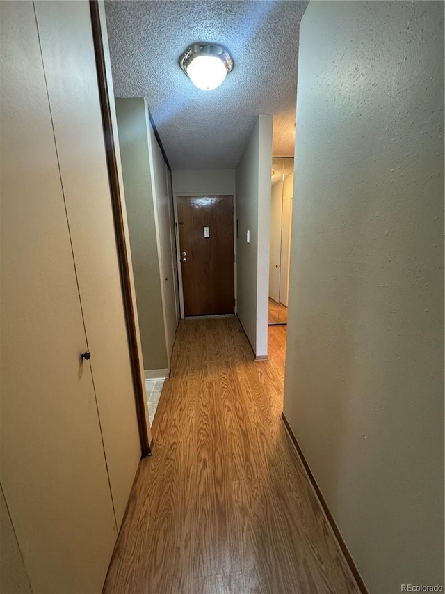hall with a textured ceiling and light wood-type flooring